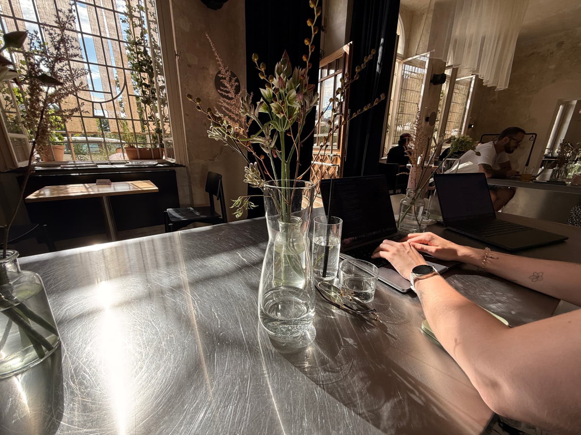 Laptops and flowers on a steel table in a sunlit Prague space