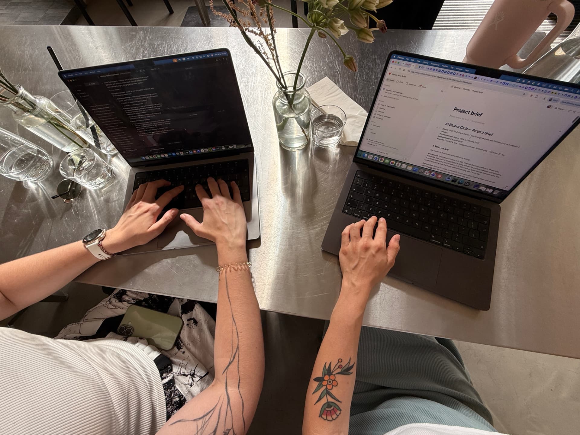 Two members working side by side on laptops at a steel table